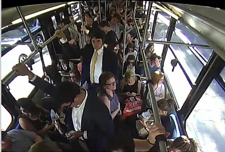 Overhead photo from inside a bus. Every seat is occupied and there are people standing shoulder-to-shoulder in the aisles.
