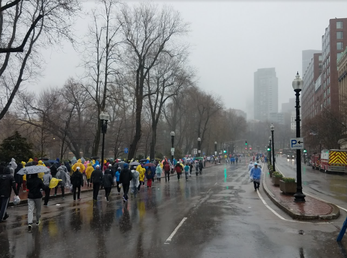 A crowd of spectators with umbrellas walk along the Boston Common during Boston Marathon 2018